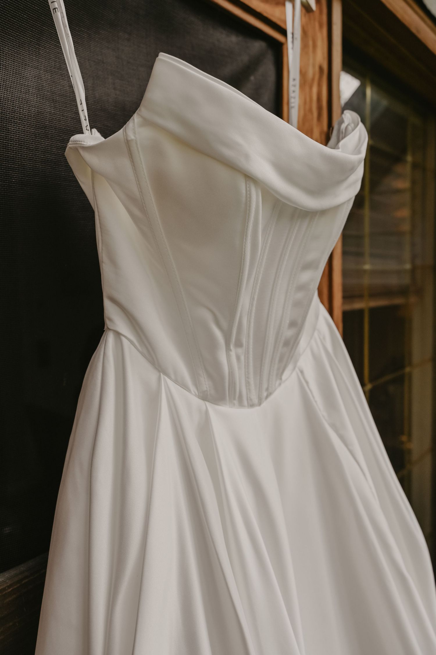 Close-up detail of a white strapless wedding dress bodice with structured corset design hanging on display.