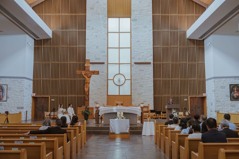 Modern church interior with wooden beams, white walls, and crucifix at altar.