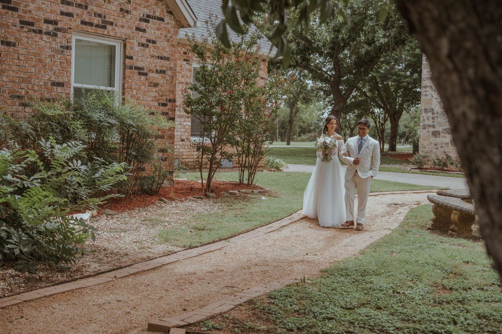 Couple walks along garden path with brick wall and green foliage.