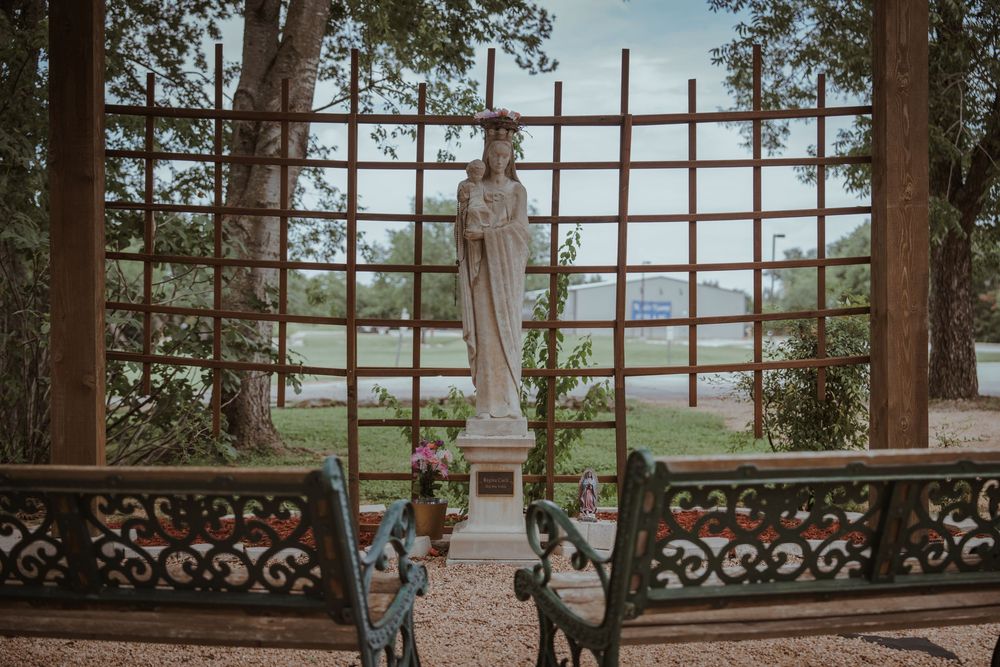 White statue stands between ornate metal benches in a garden setting with mountain views in the background.
