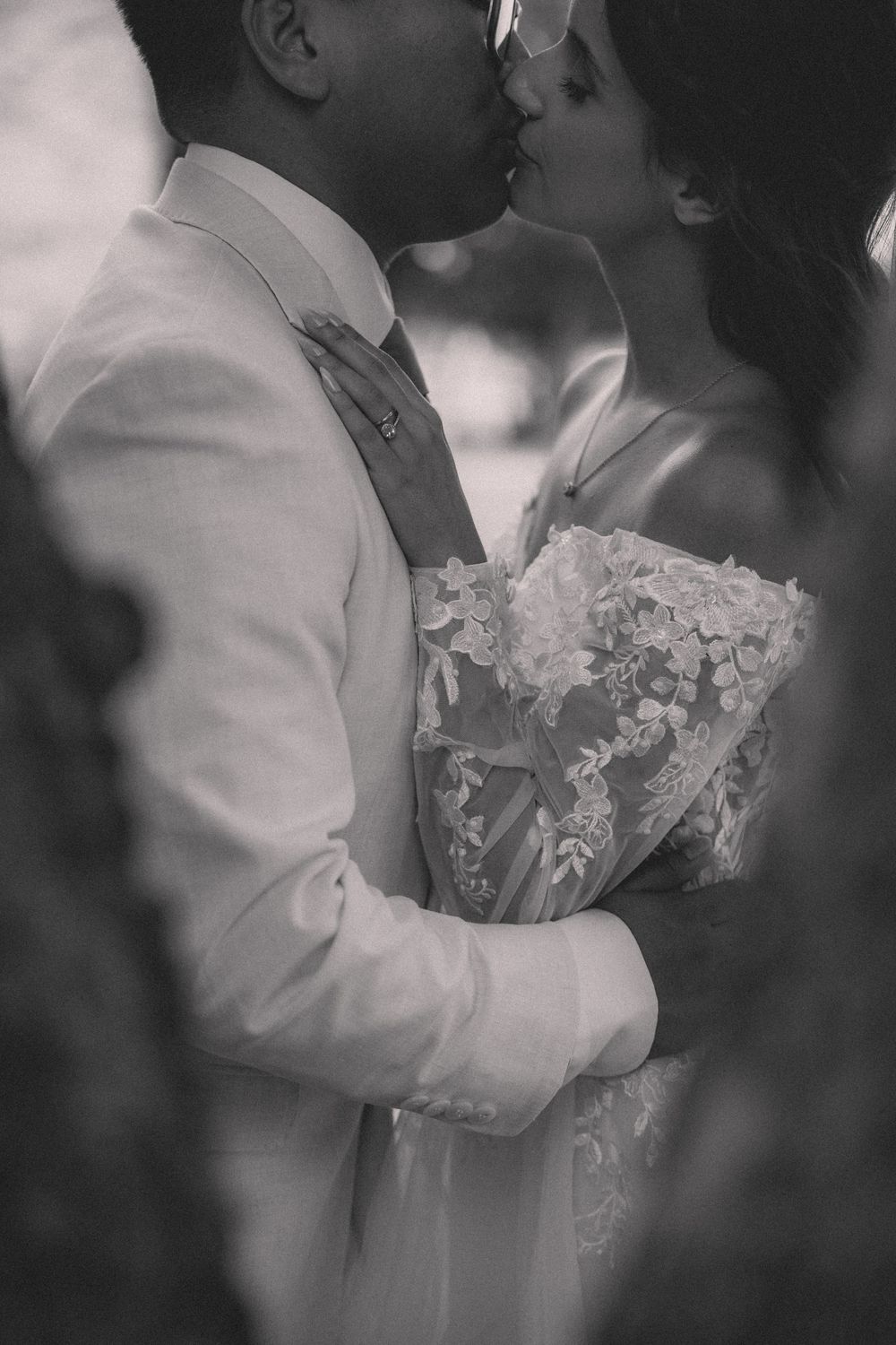Intimate black and white portrait of newlyweds in white attire sharing a tender moment.