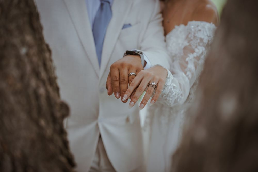 Close-up of wedding rings and lace details on hands against white attire.