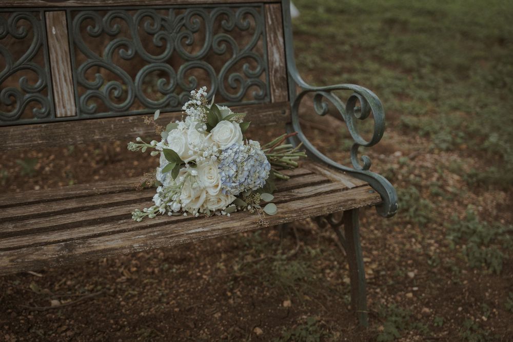 White and blue wedding bouquet rests on an ornate metal garden bench.
