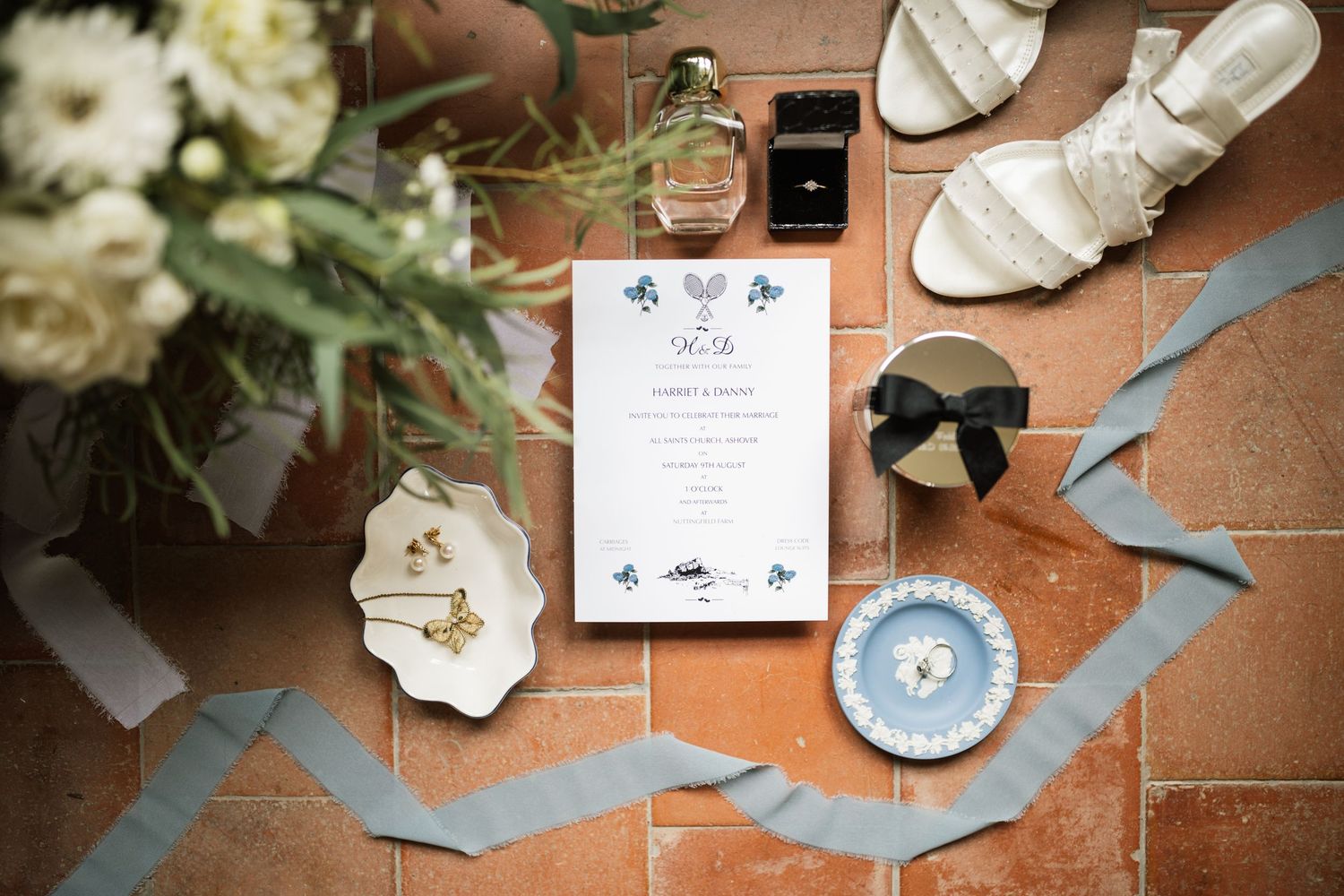 A collection of wedding details including invitations, ribbons, and floral arrangements laid out on a terracotta surface.