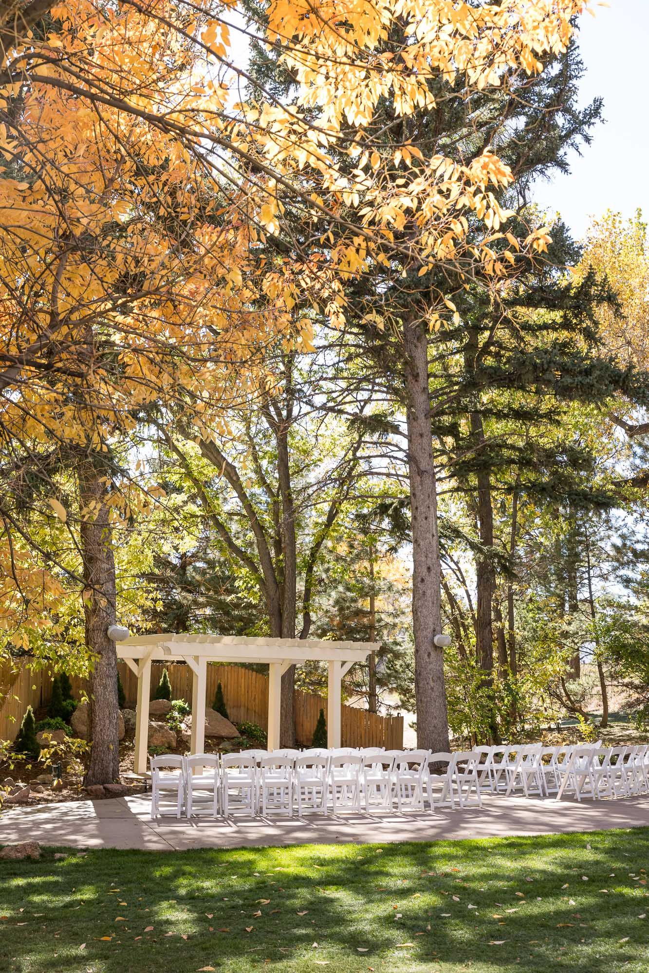 Outdoor wedding ceremony setup with rows of white chairs along a curved path surrounded by evergreen trees and shrubs.
