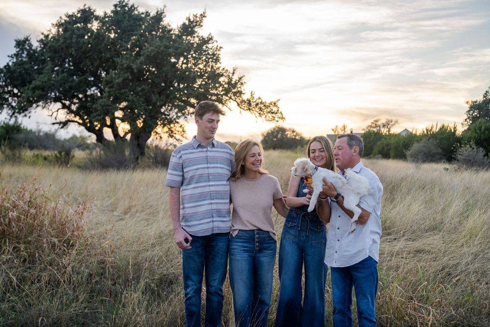 A family poses together in a golden field at sunset with a large tree in the background.