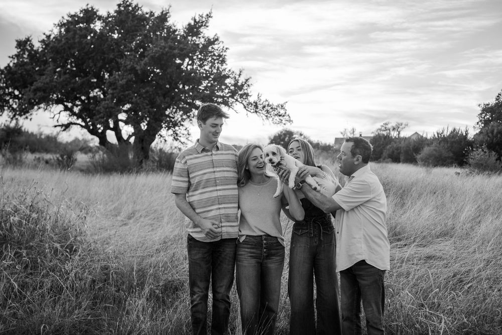 Black and white photo of a group sharing laughter in a grassy field with a tree backdrop.