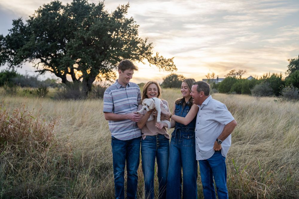 A group laughs together while standing in tall grass during golden hour.