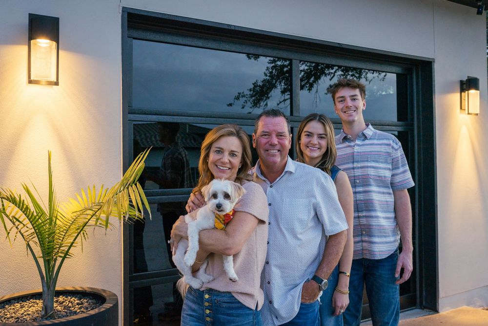 A family stands together on their porch holding a small white dog.