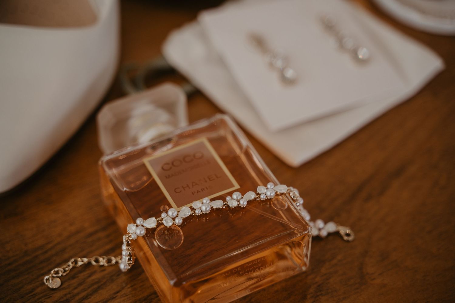 Perfume bottles and jewelry arranged on a wooden surface in warm lighting.