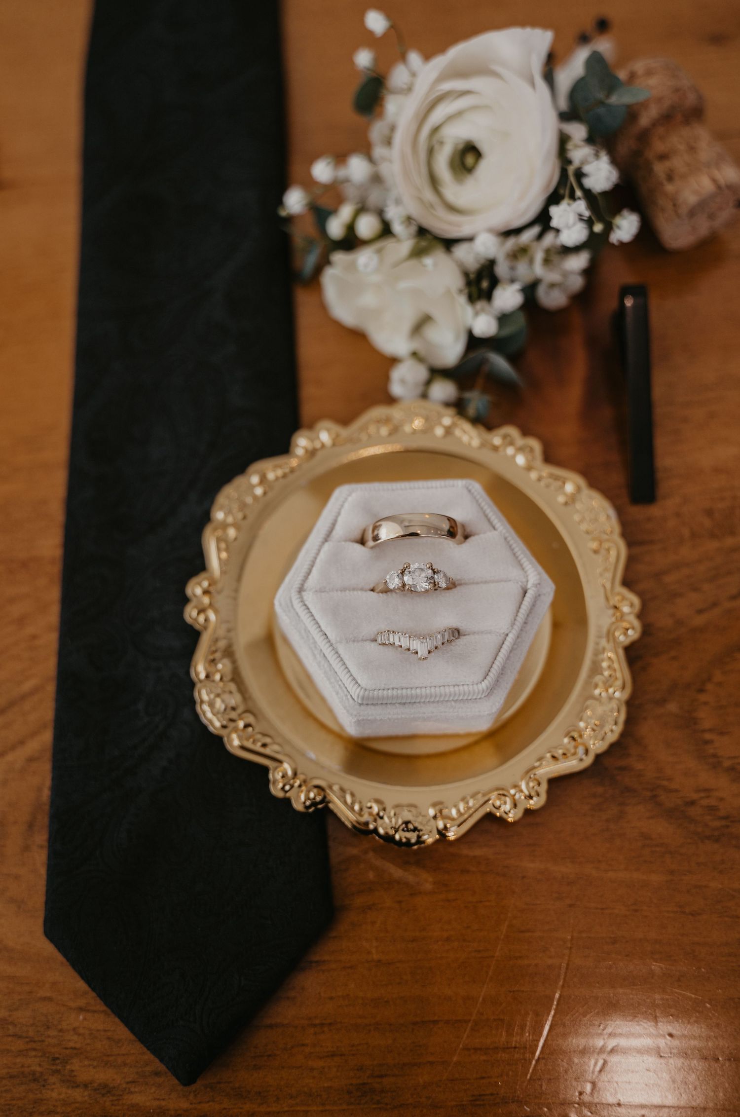 Wedding rings displayed on elegant gold-rimmed hexagonal holders with delicate floral accents on wooden surface.