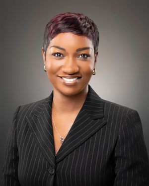 Professional portrait of a person in a pinstriped black blazer smiling warmly against a grey background.