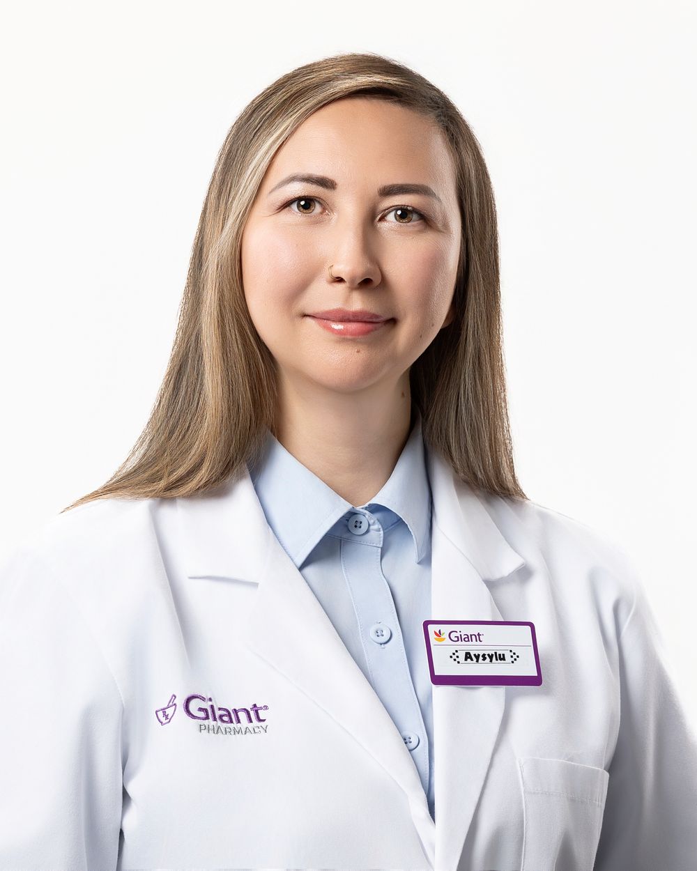 Healthcare professional in white lab coat and light blue collared shirt posing for portrait against white background.