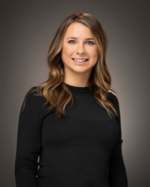 Professional headshot portrait of someone wearing a black turtleneck sweater against a dark gray studio background.