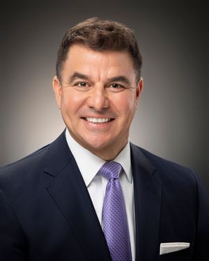 Professional headshot of person in dark suit and purple tie against gradient background.
