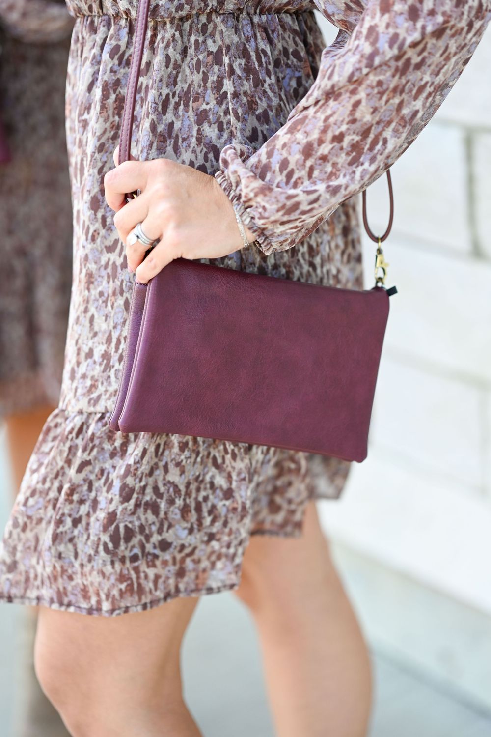 Close-up of burgundy leather clutch bag held against floral print dress.