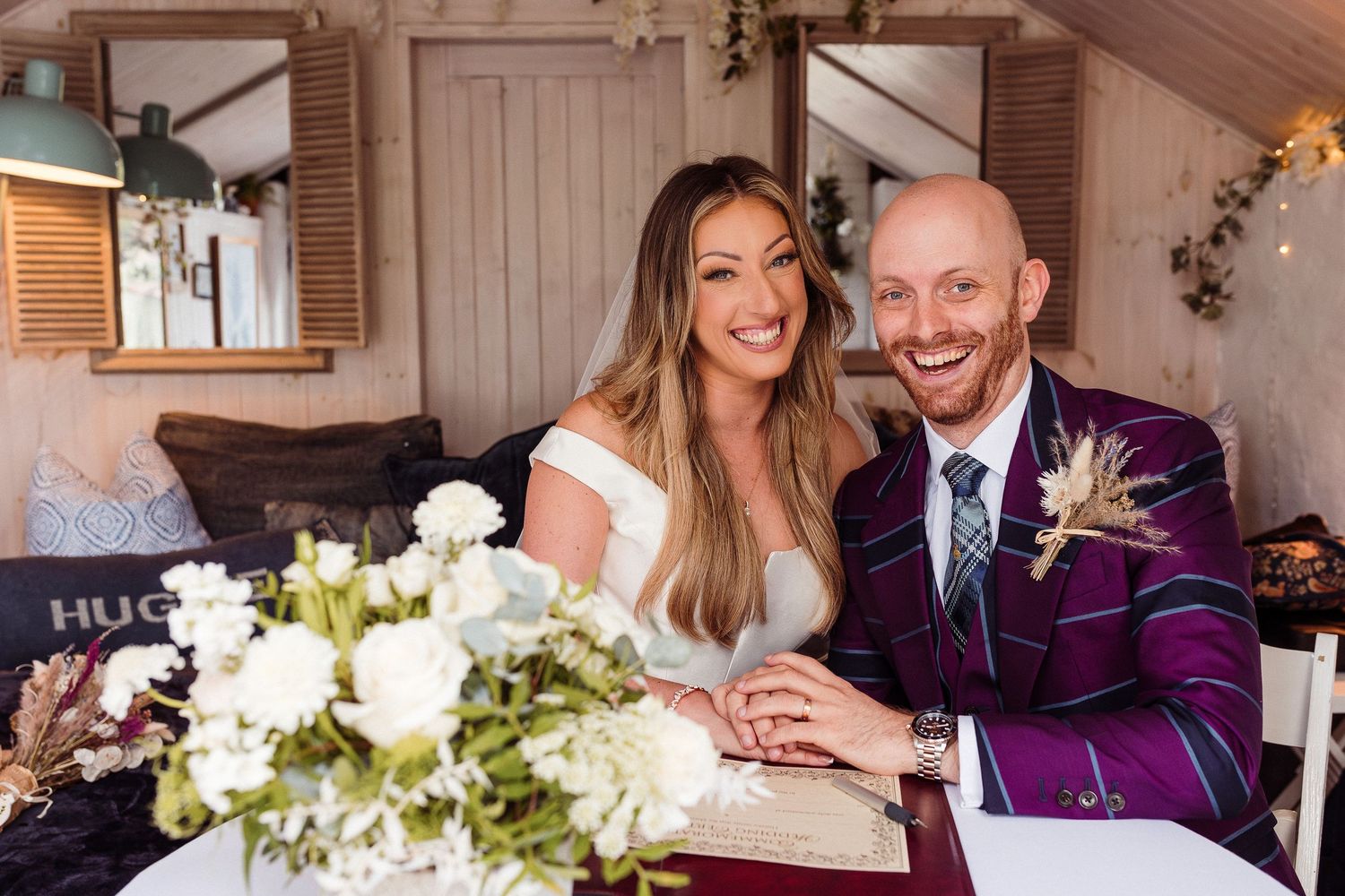A bride and groom pose for a photo at a reception table decorated with white floral arrangements and candles at Gilpin Hotel and Lake House.