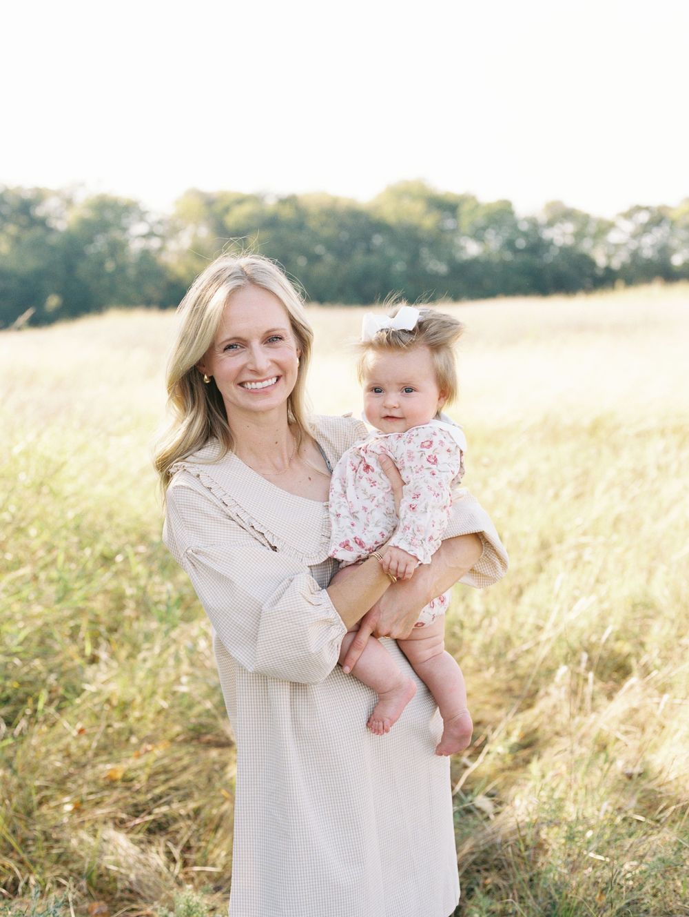 Mother and baby share tender moments in a sun-drenched field during golden hour photoshoot.