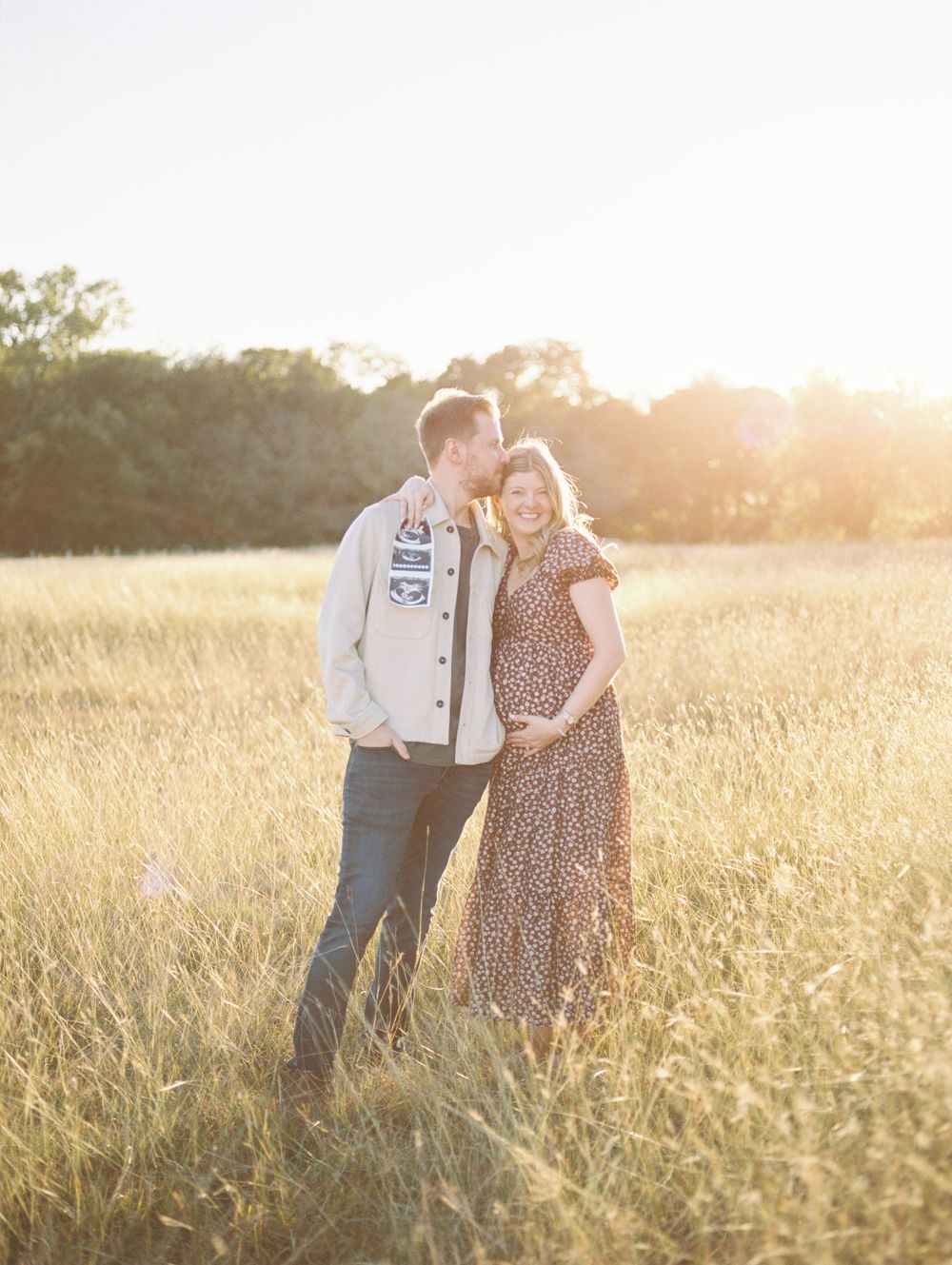 A couple embraces in a sun-drenched field of tall grass during golden hour creating a romantic silhouette.