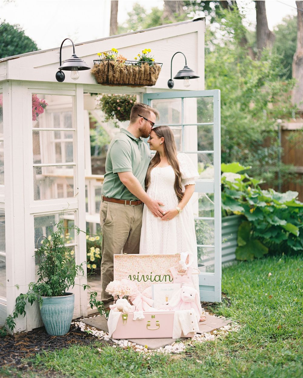 A romantic couple stands together in front of a rustic greenhouse with vintage decor and garden elements in a backyard setting.