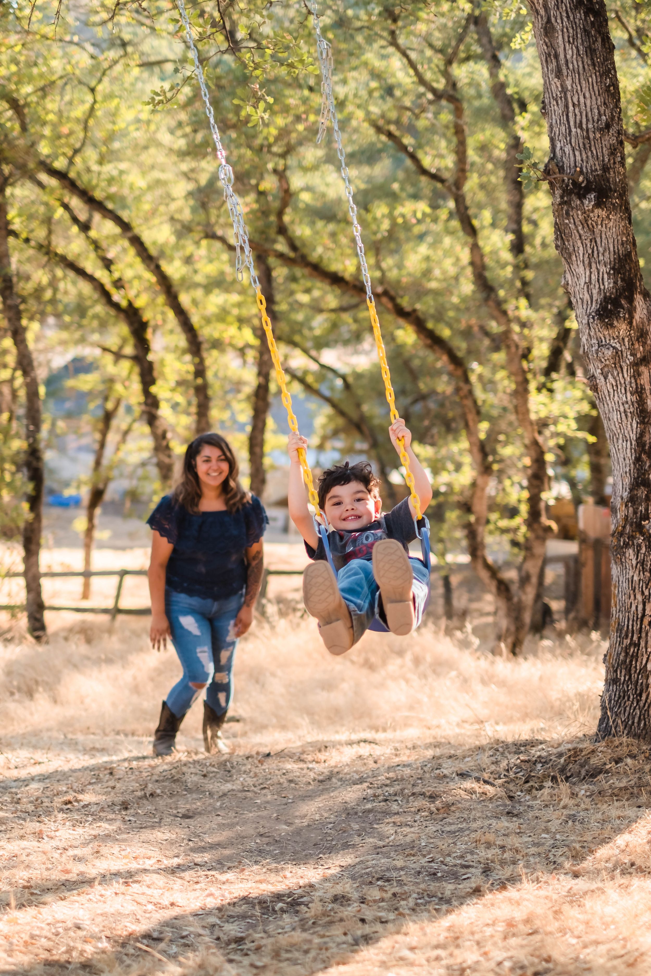A child swings joyfully on a rope swing in a sunlit wooded area during a warm summer day in valley springs ca