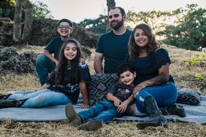 A family relaxes outdoors on a blanket during golden hour while taking casual photos together in nature.