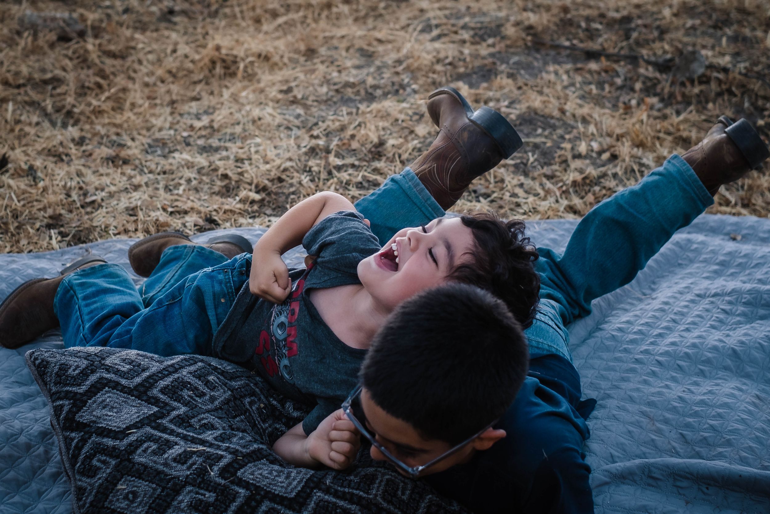 A younger brother plays with his siblings on a blanket in his front yard in valley springs ca