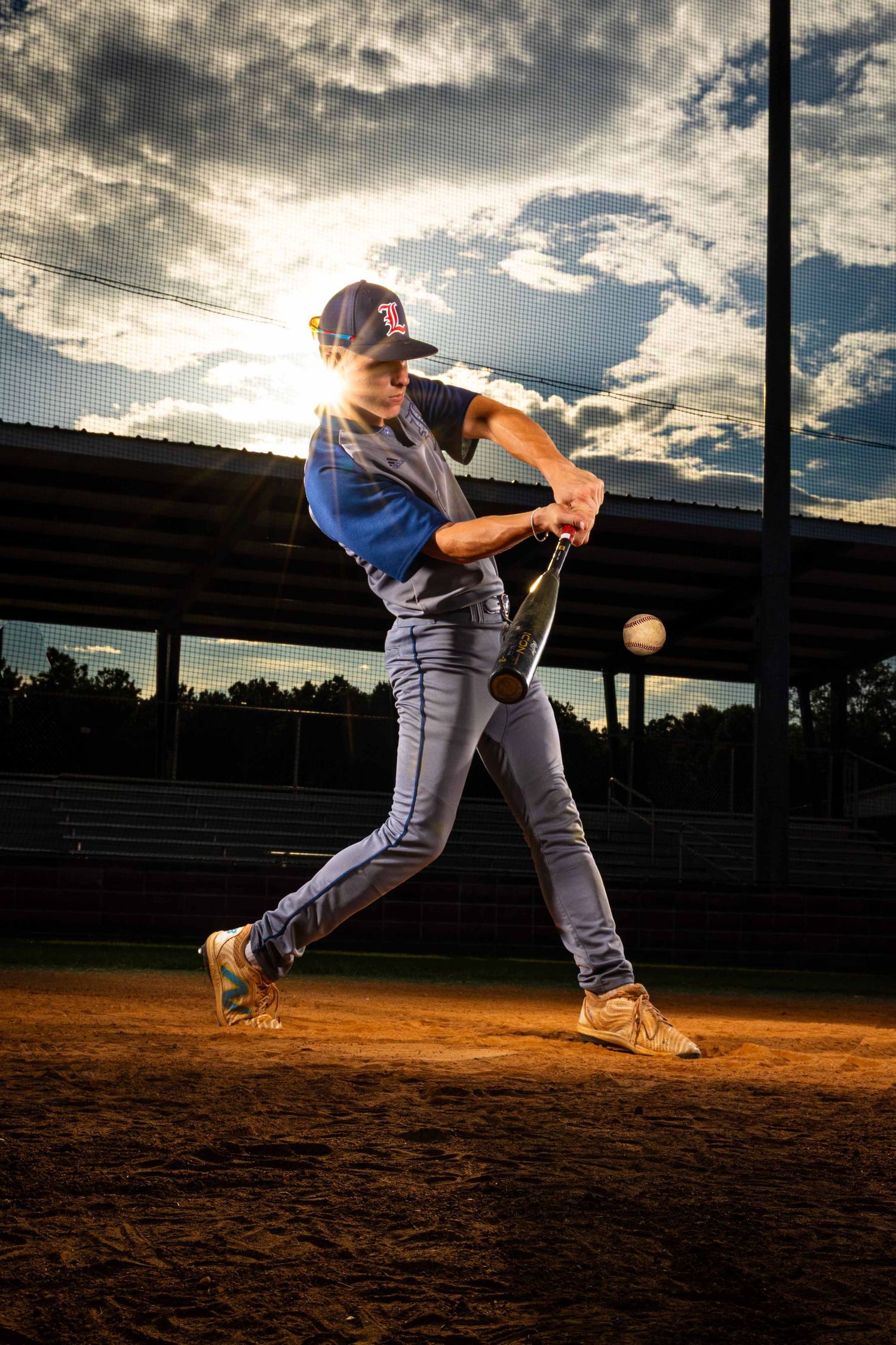 Baseball player swings bat at sunset in dramatic multi-frame sequence showing follow-through motion on dirt field.