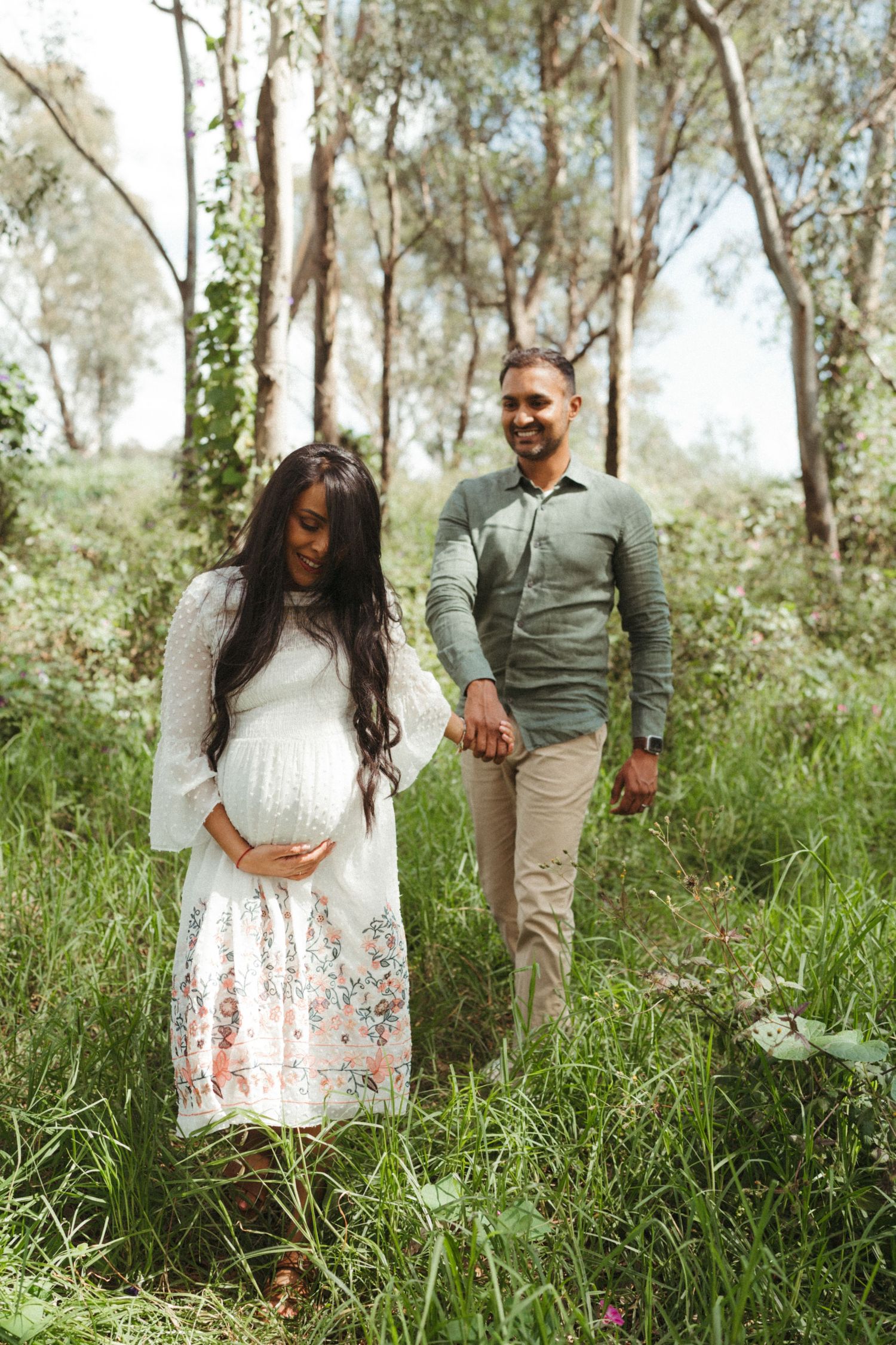 Expectant couple sharing intimate moment in forest setting with tall eucalyptus trees.