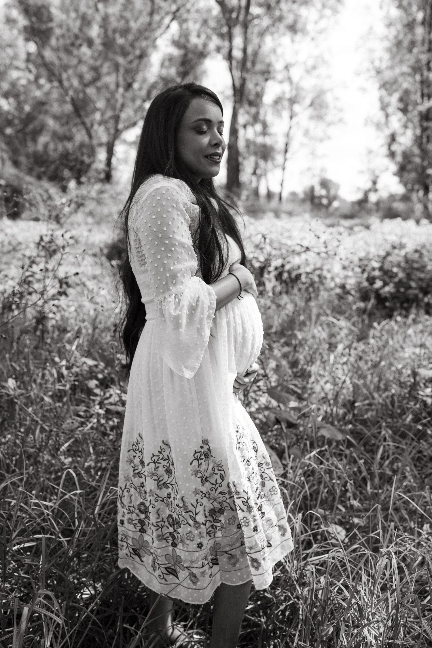 Black and white maternity photos showing a flowing white dress in a natural outdoor setting.