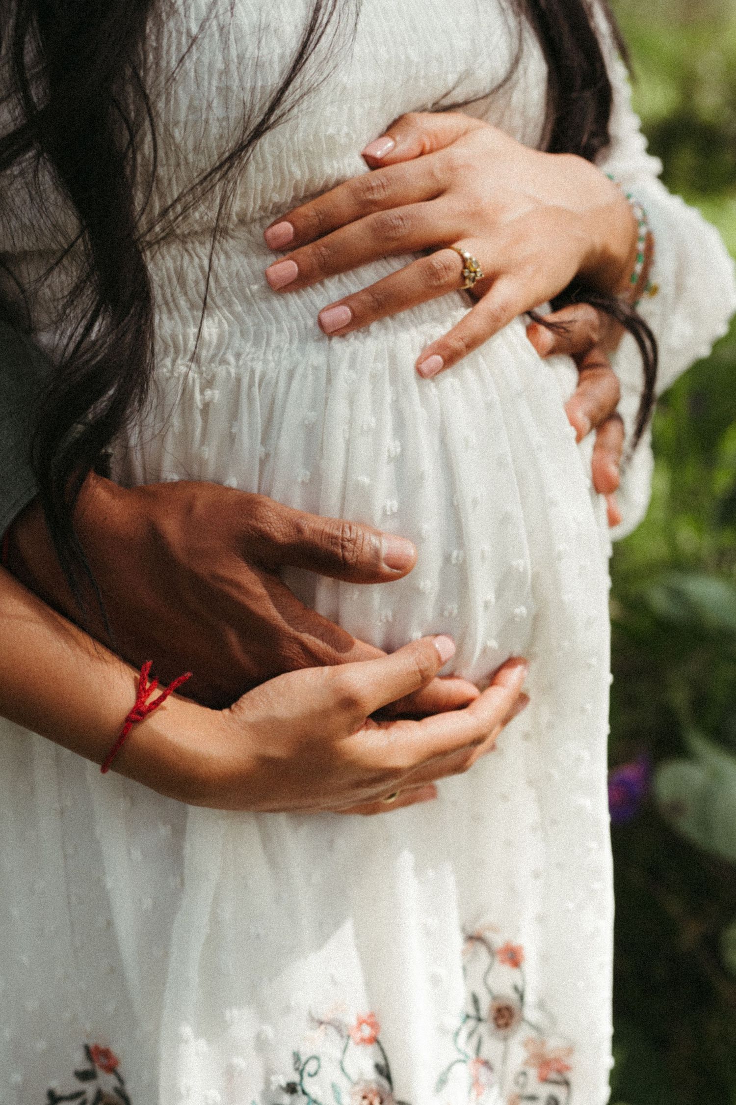 Close-up shots of hands gently cradling a pregnant belly in a white lace dress.