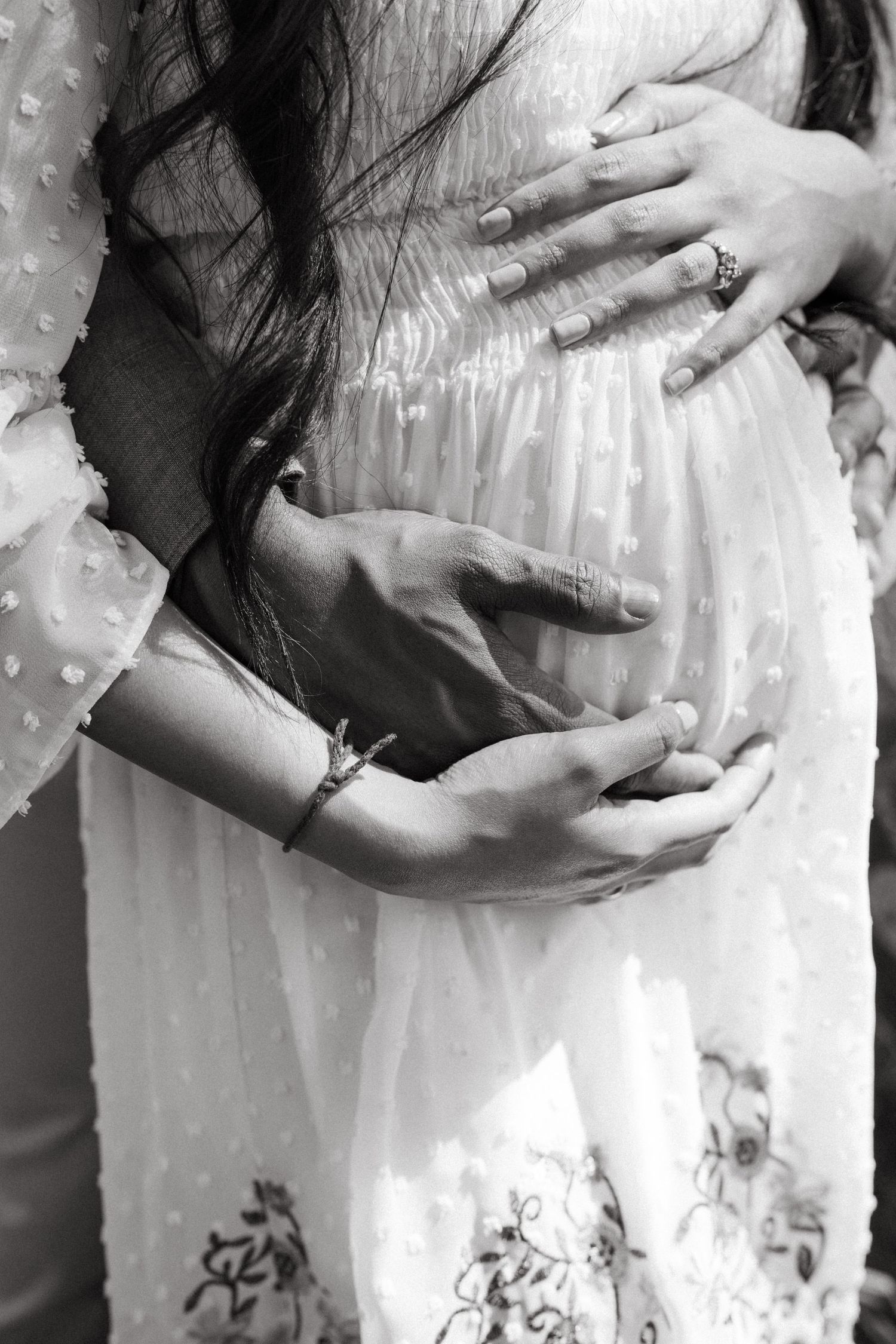 Artistic close-up series of hands tenderly holding a pregnant belly in white lace.