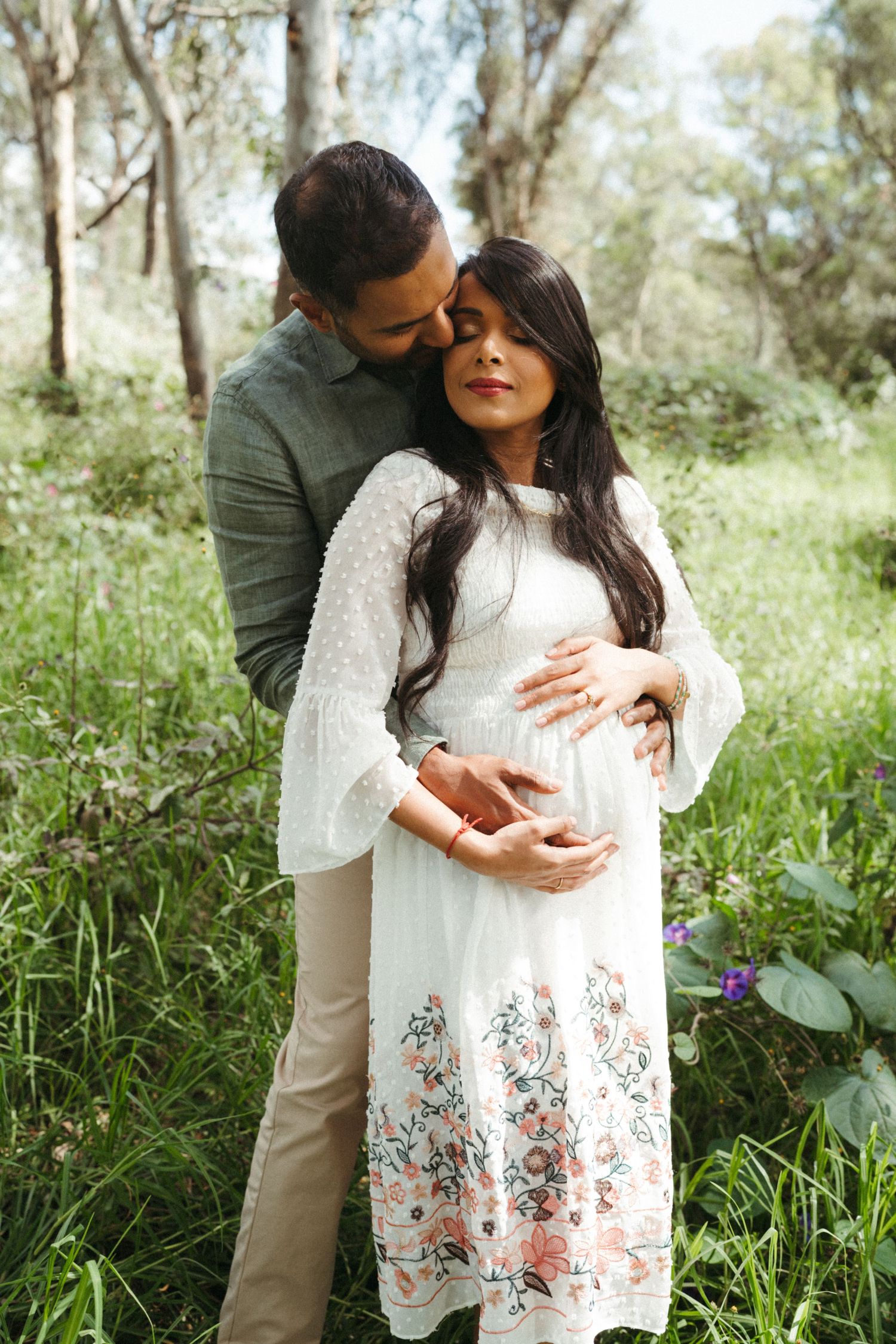 Intimate maternity photos in a grassy field with couple embracing.
