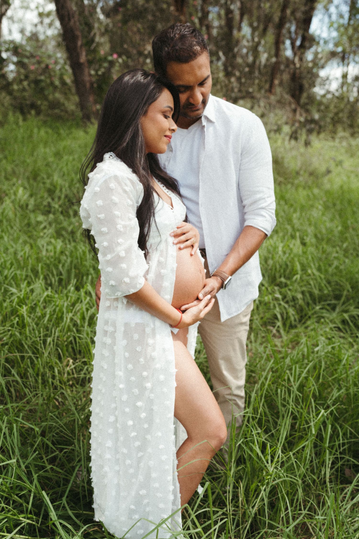 Outdoor maternity session showing couple in white clothing among tall grass.