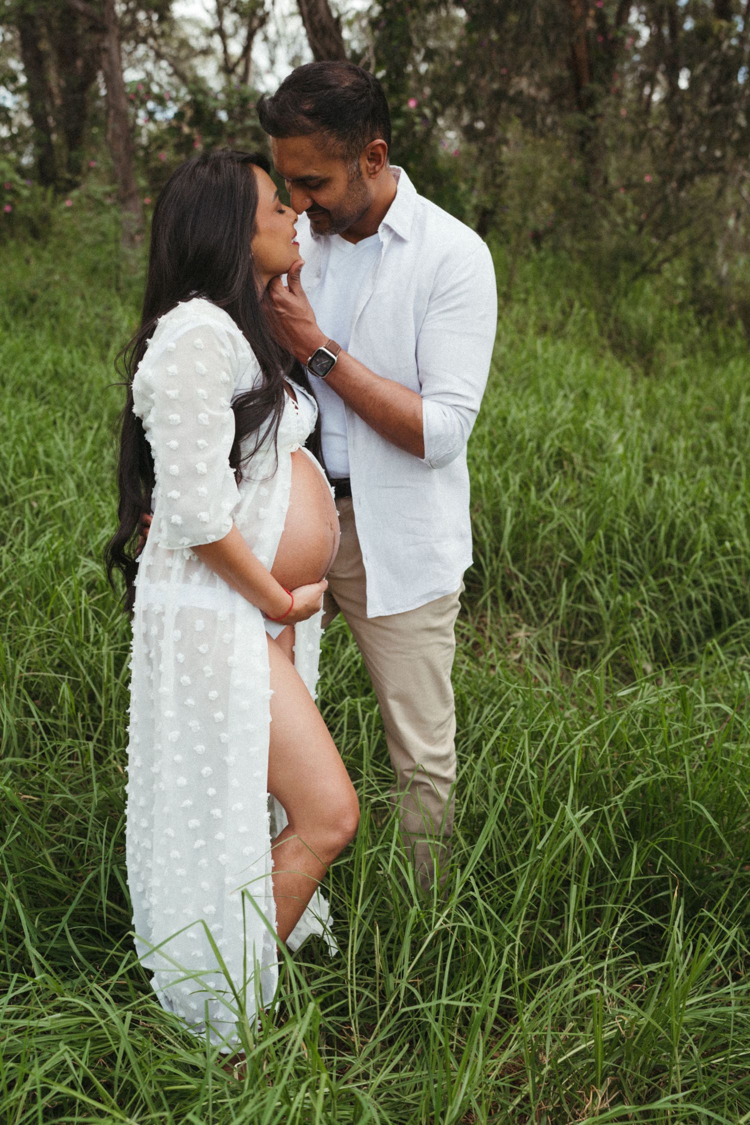 Intimate maternity portraits in a natural setting with tall grass and trees.