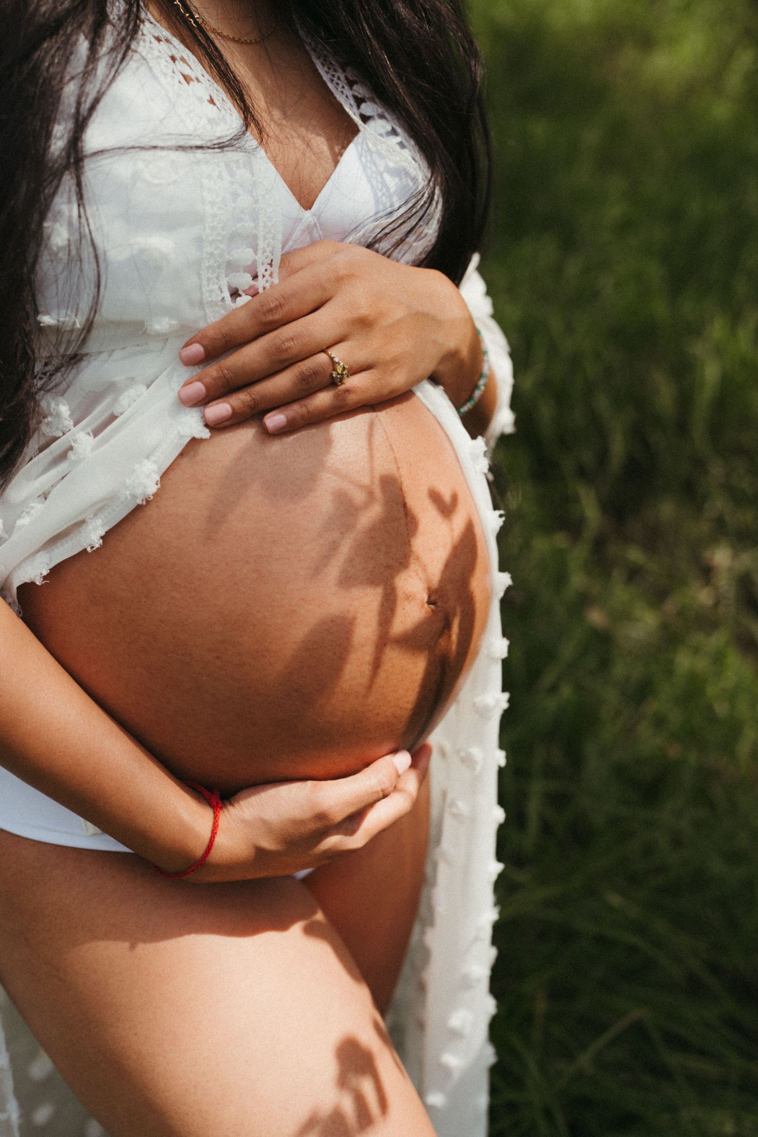 Sunlit maternity photos focusing on gentle hands cradling pregnant belly.