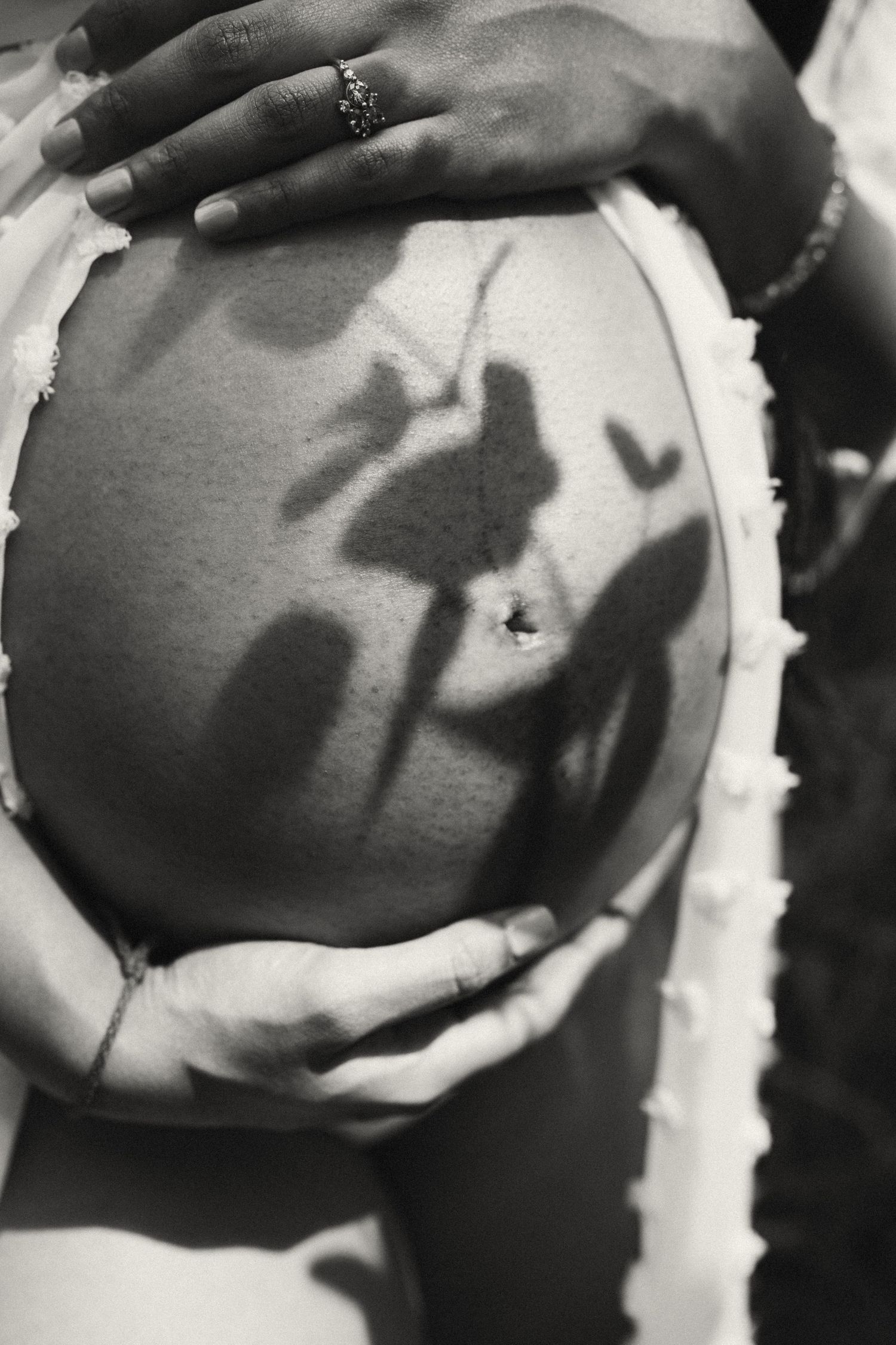 Black and white artistic close-ups of hands on pregnant belly with shadow play.