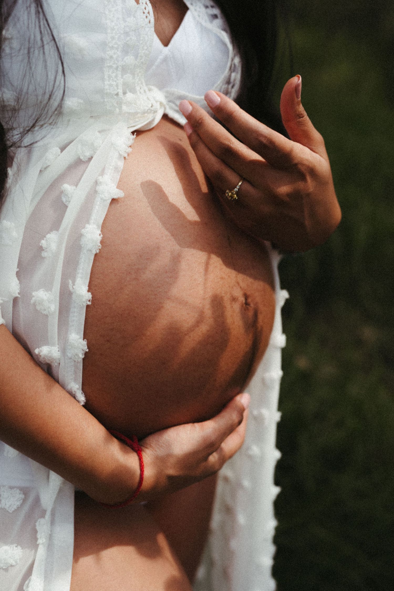 A close-up maternity photo showing a pregnant belly with a delicate white lace dress.