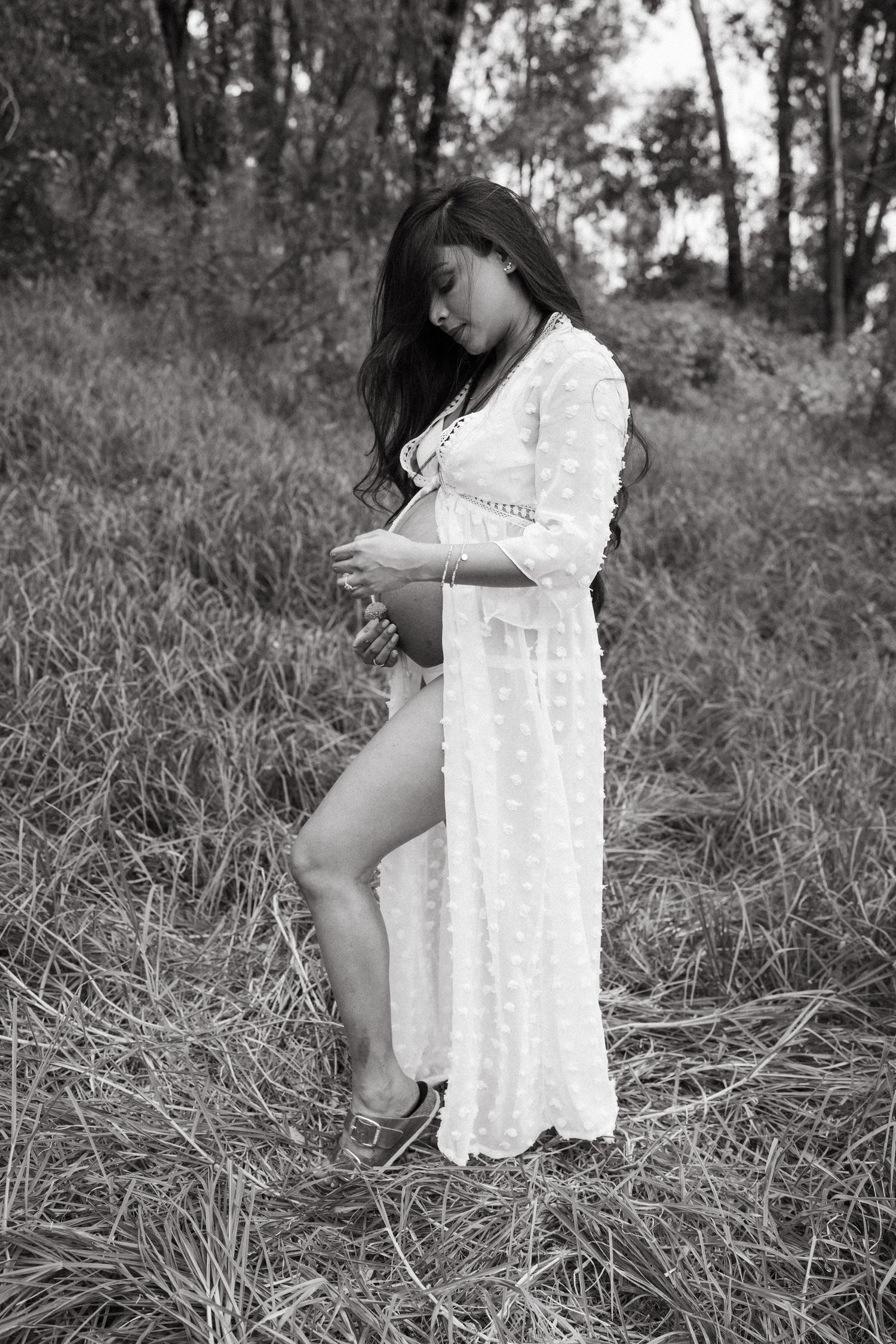 Black and white maternity portrait in a natural outdoor setting with tall grass.
