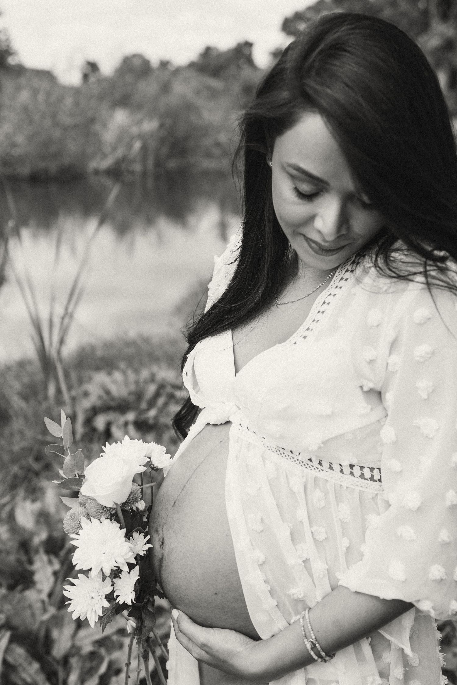 Black and white maternity portrait with white flowers and a dotted lace dress.
