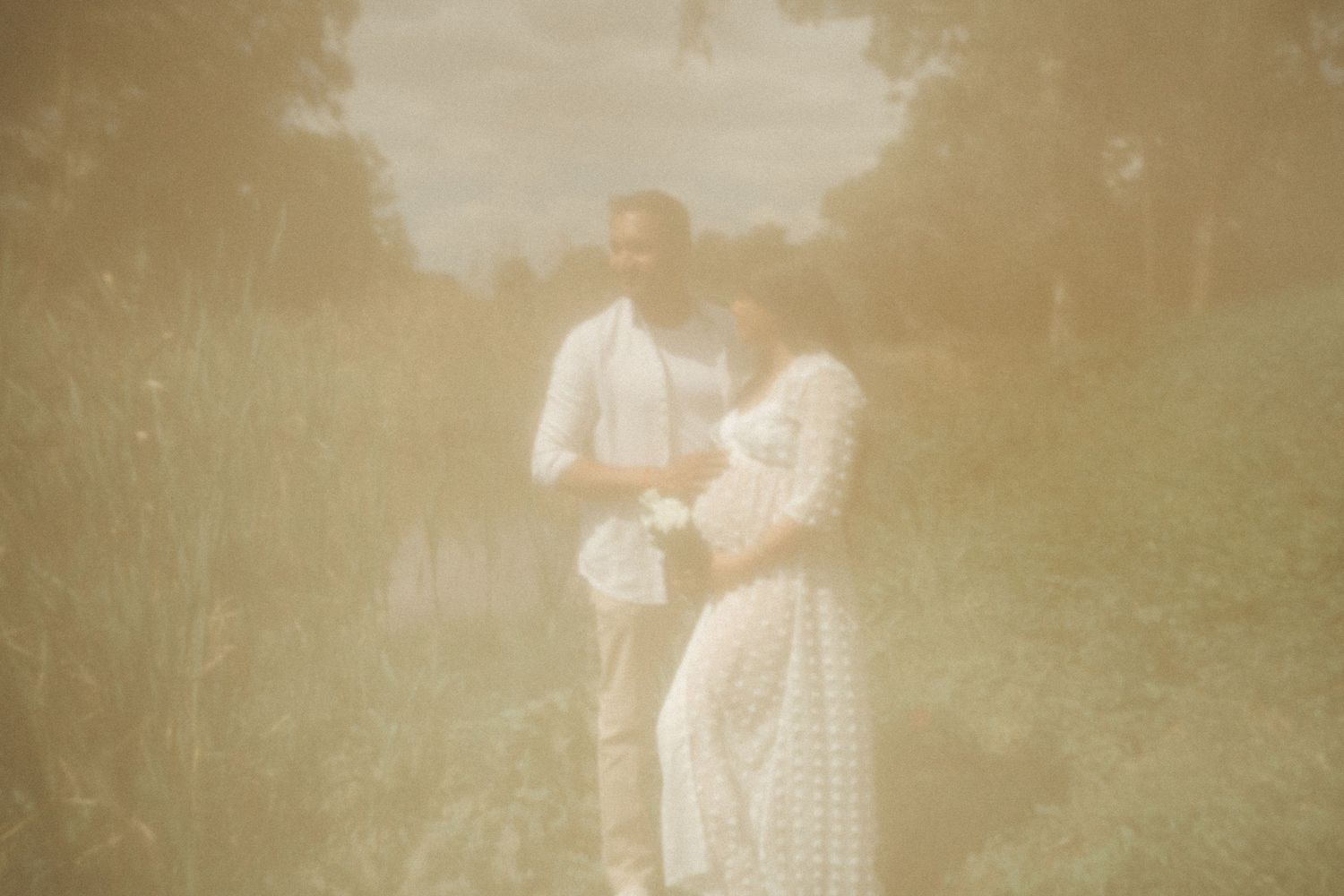 Dreamy sepia maternity photo with soft focus and natural outdoor lighting.
