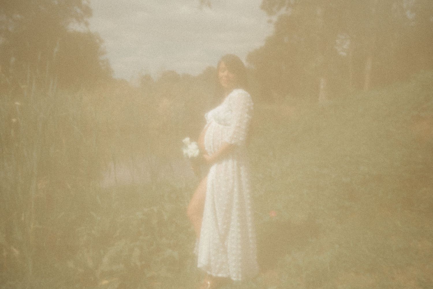 Dreamy ethereal portrait of someone in a white dress standing in a misty field.