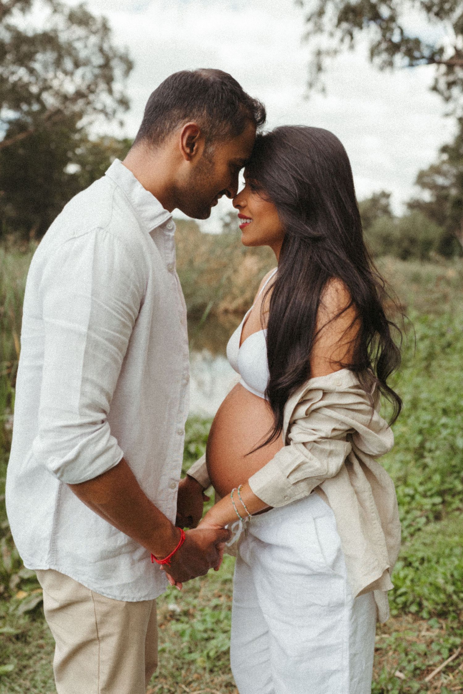 Intimate maternity photo of a couple embracing outdoors in casual white clothing.
