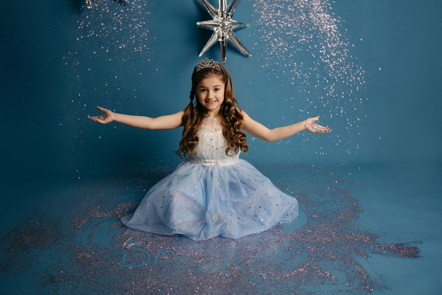 A young girl in a blue princess dress twirls gracefully against a dreamy blue backdrop with falling glitter.