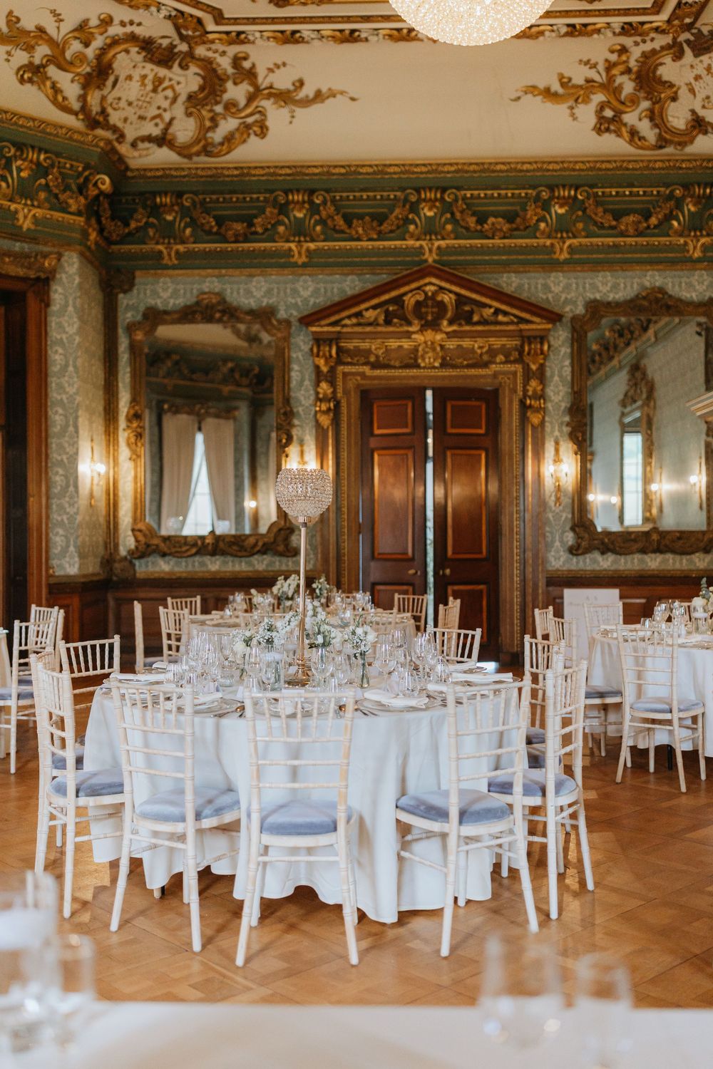 Elegant ballroom with ornate gold ceiling details and white round tables set for a formal wedding reception.