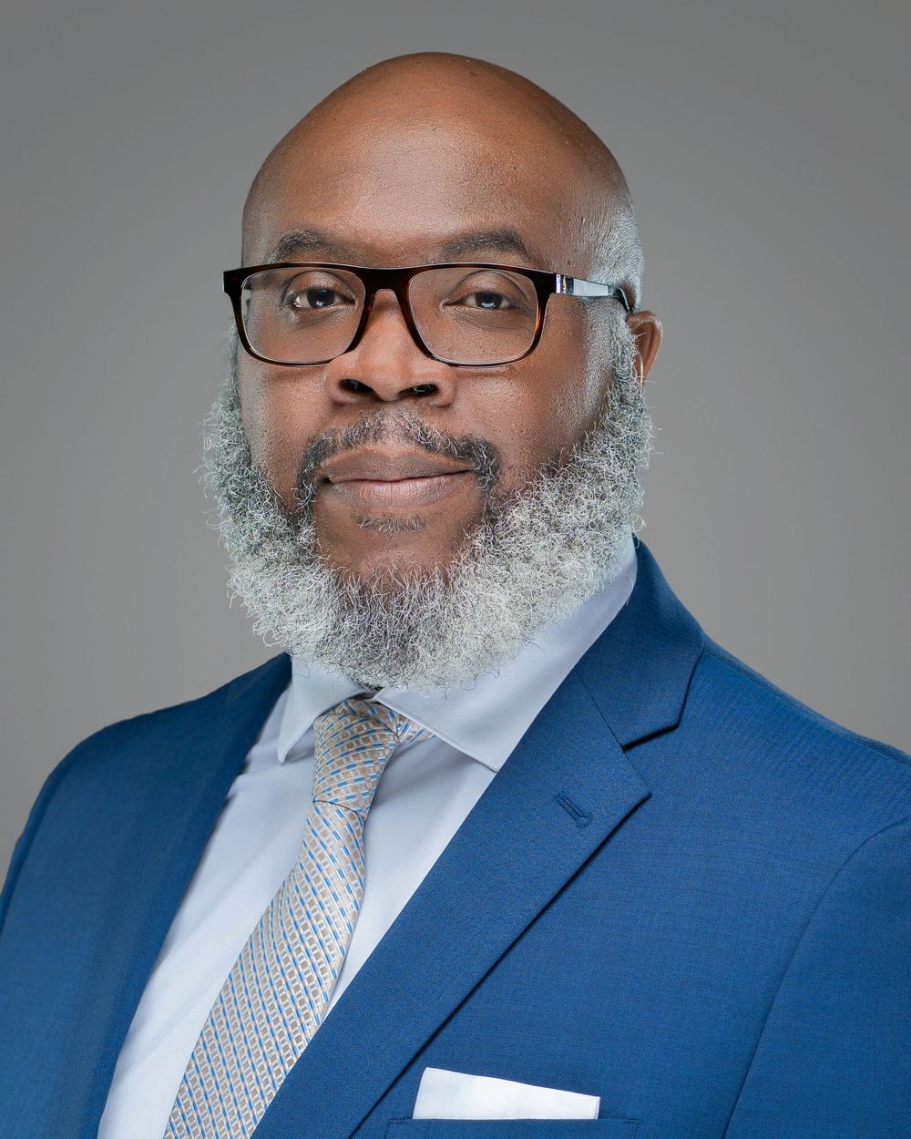 Professional headshots of someone wearing a blue suit and glasses against a gray backdrop. Kelly Photography Atlanta Headshot Session