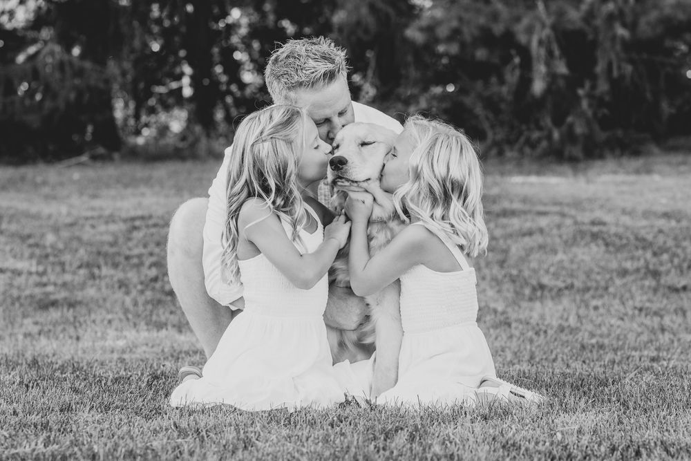 Sweet moment between dog and family on grassy field in black and white photo.