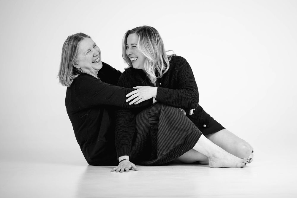 Two people sharing joyful laughter while sitting together in black sweaters on white background.