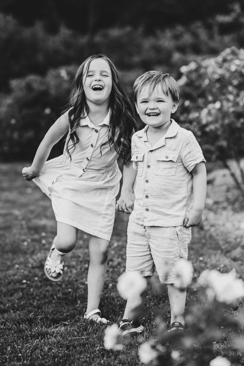 Two children laughing and playing together outdoors in black and white photography.
