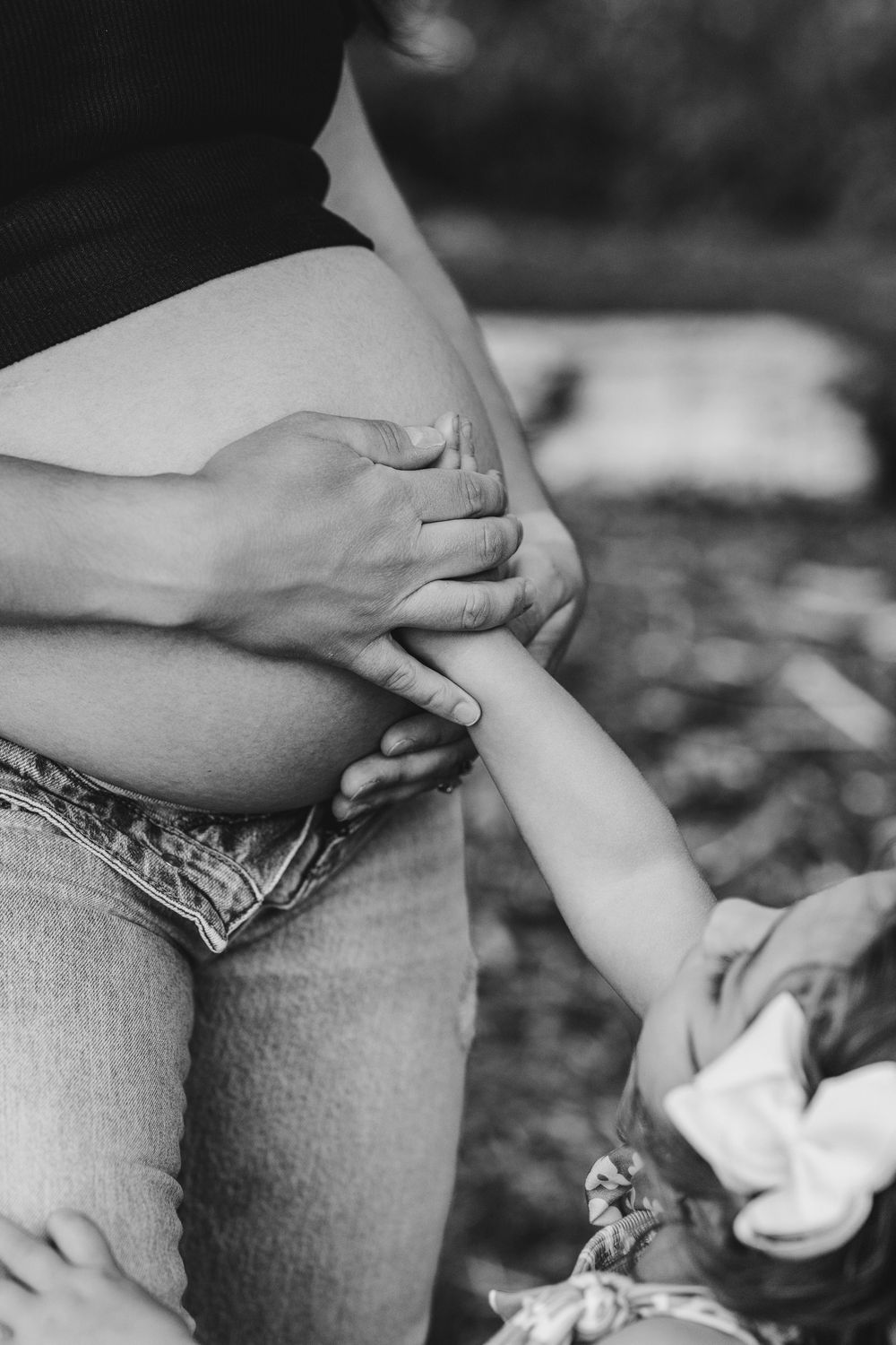Black and white photo of a pregnant woman outdoors, with a child gently touching her baby bump.